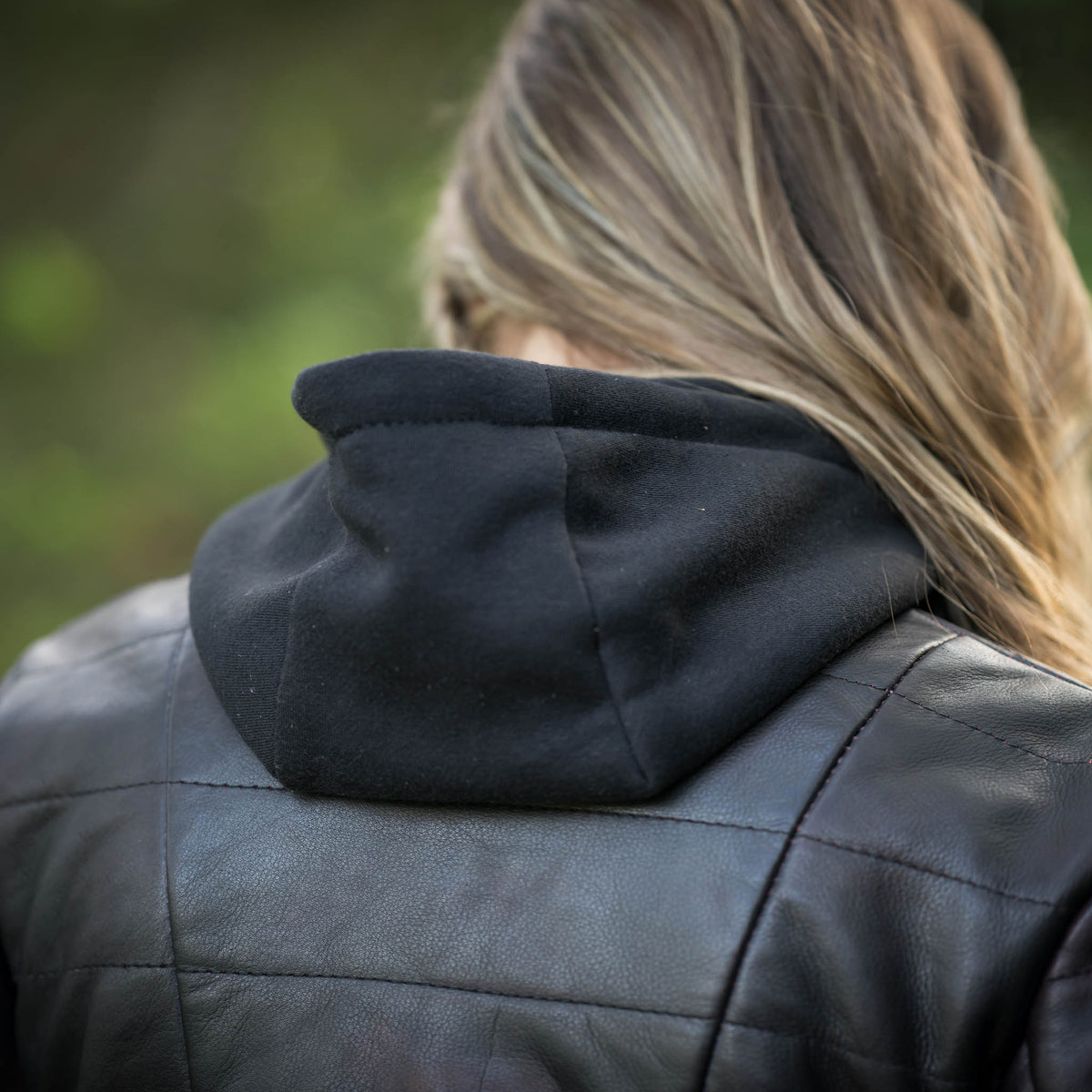 Person wearing a black quilted jacket with a blurred green background.