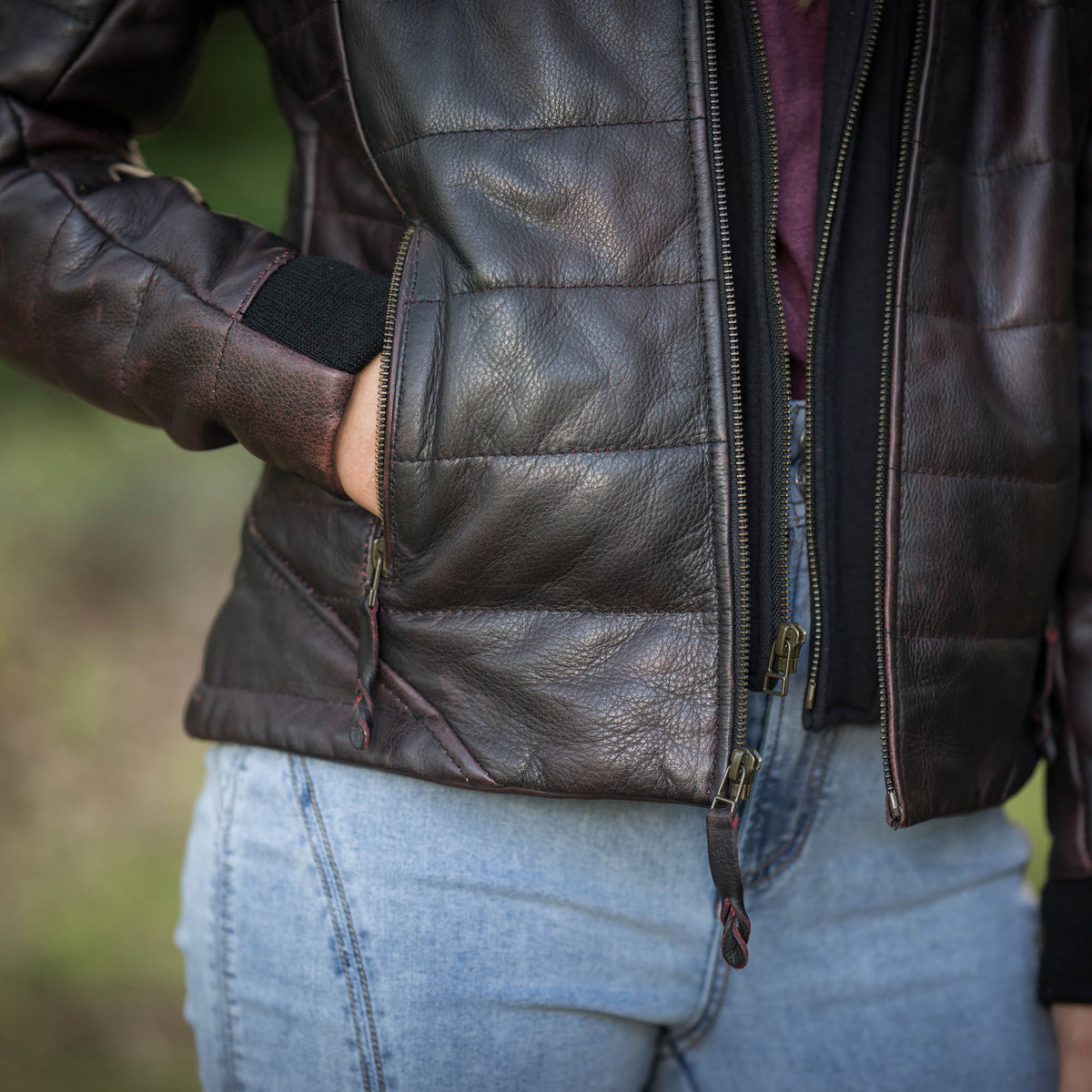 Person wearing a black leather jacket and blue jeans with a blurred background.