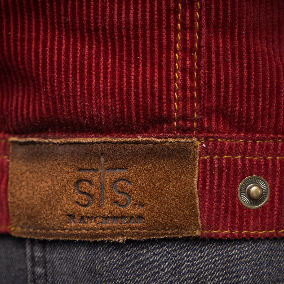 closeup of the rough out patch with sts logo on our red cotton corduroy snap closure jacket with two chest pockets and leather collar details