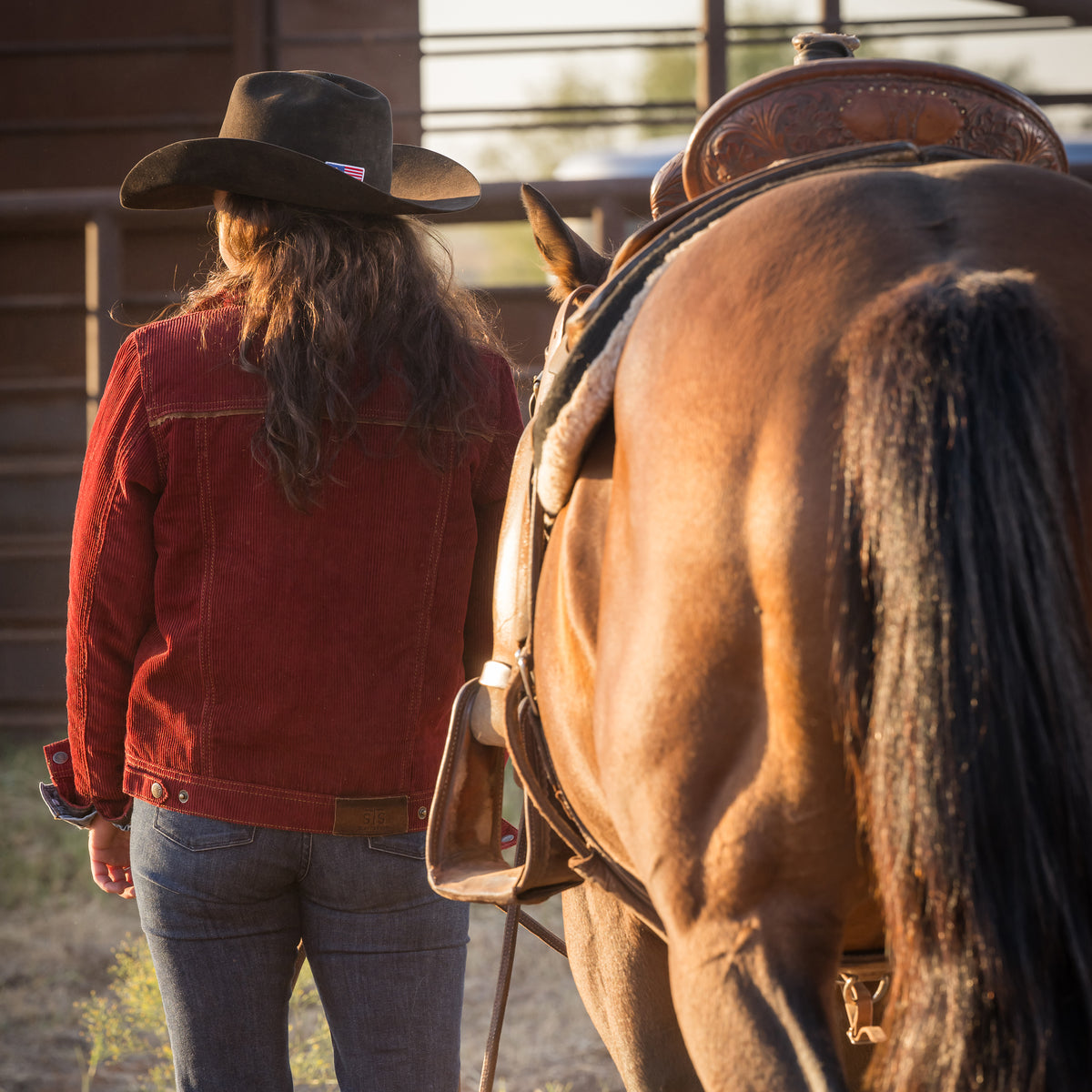 back of a woman wearing our red cotton corduroy snap closure jacket with two chest pockets and leather collar details next to a brown horse