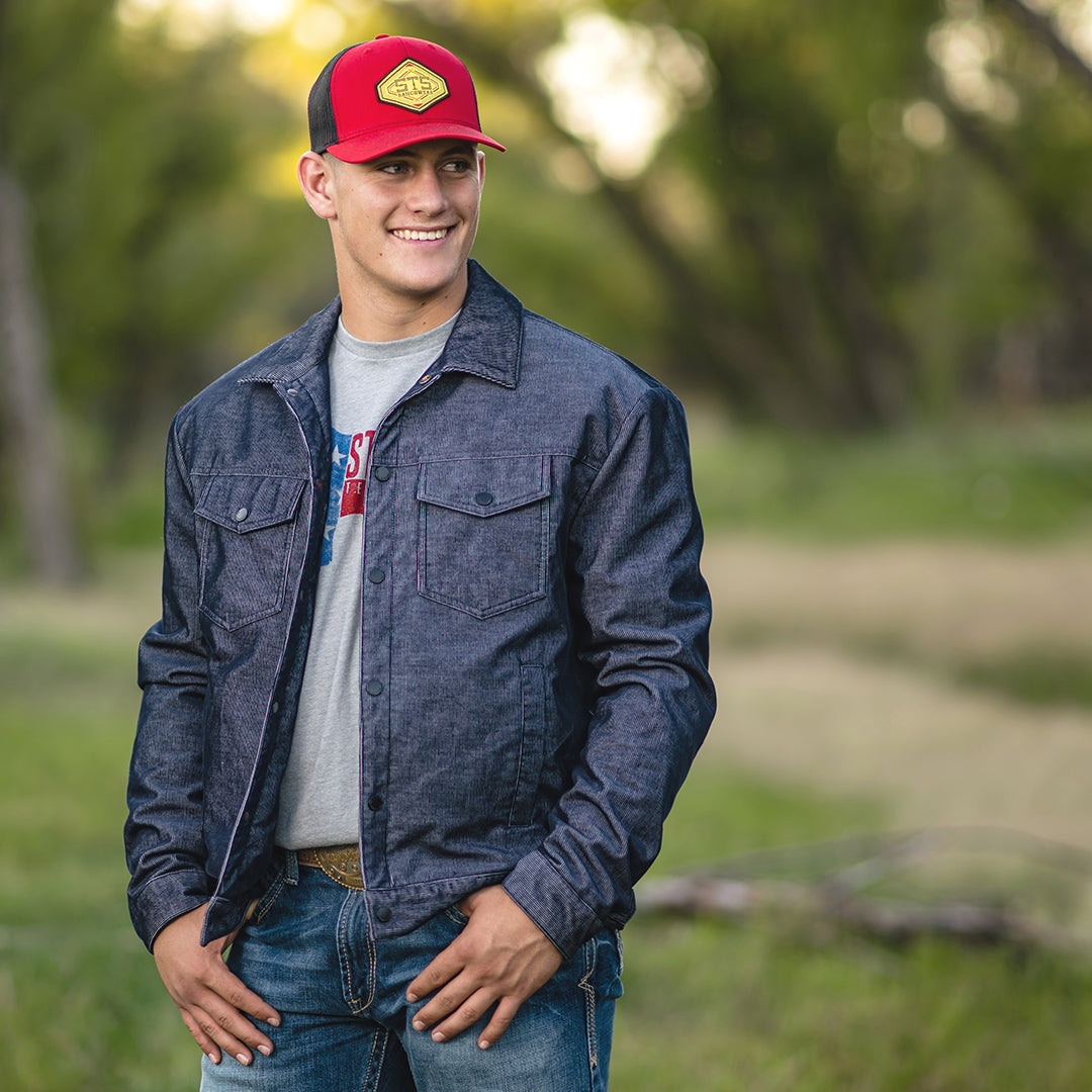 Man standing in a forest setting wearing a red hat and corduroy jacket in blue, featuring a snap front closure and multiple pockets.