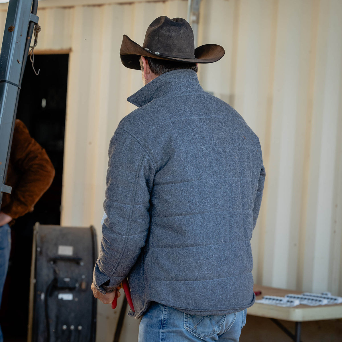 Man wearing a gray quilted wool jacket and cowboy hat in an indoor setting.