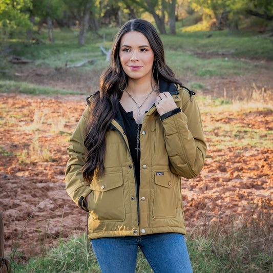 Woman wearing a brown parka jacket standing in a field with trees in the background.