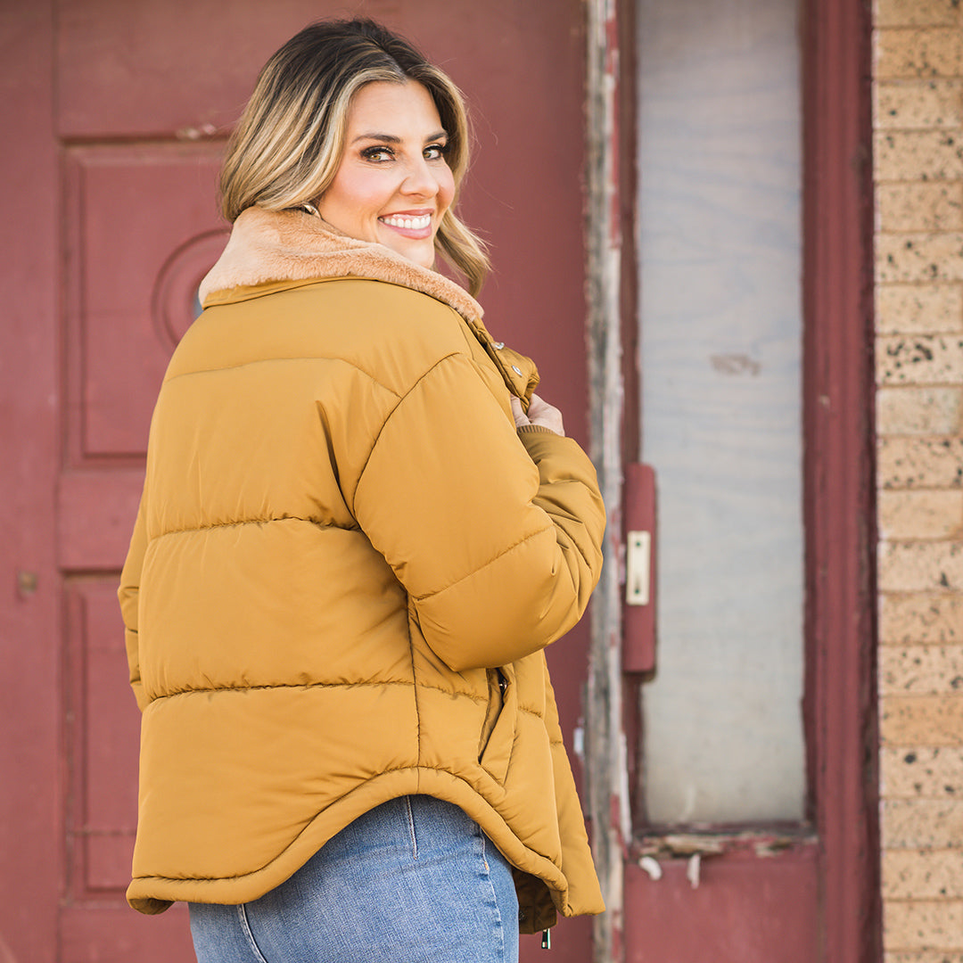 Woman in front of a red door wearing a Nova jacket in brown color with a fleece collar, zip and snap front closure and hand warming pockets.