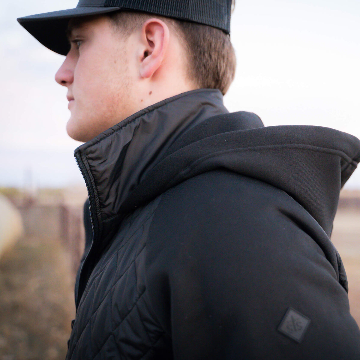 Man wearing a black hat and black quilted jacket.