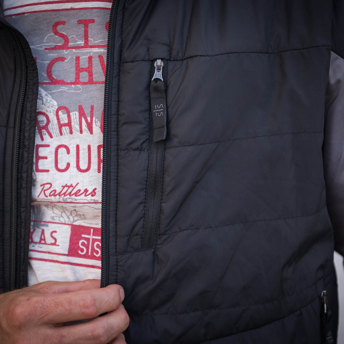 Detail of zip closure pocket with black STS zipper pull on a men's black puffy jacket.