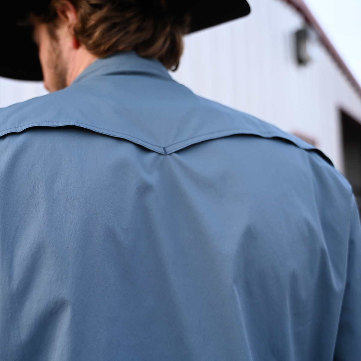 Person wearing a long-sleeved men's shirt in a solid color, featuring vents on the back shoulders.