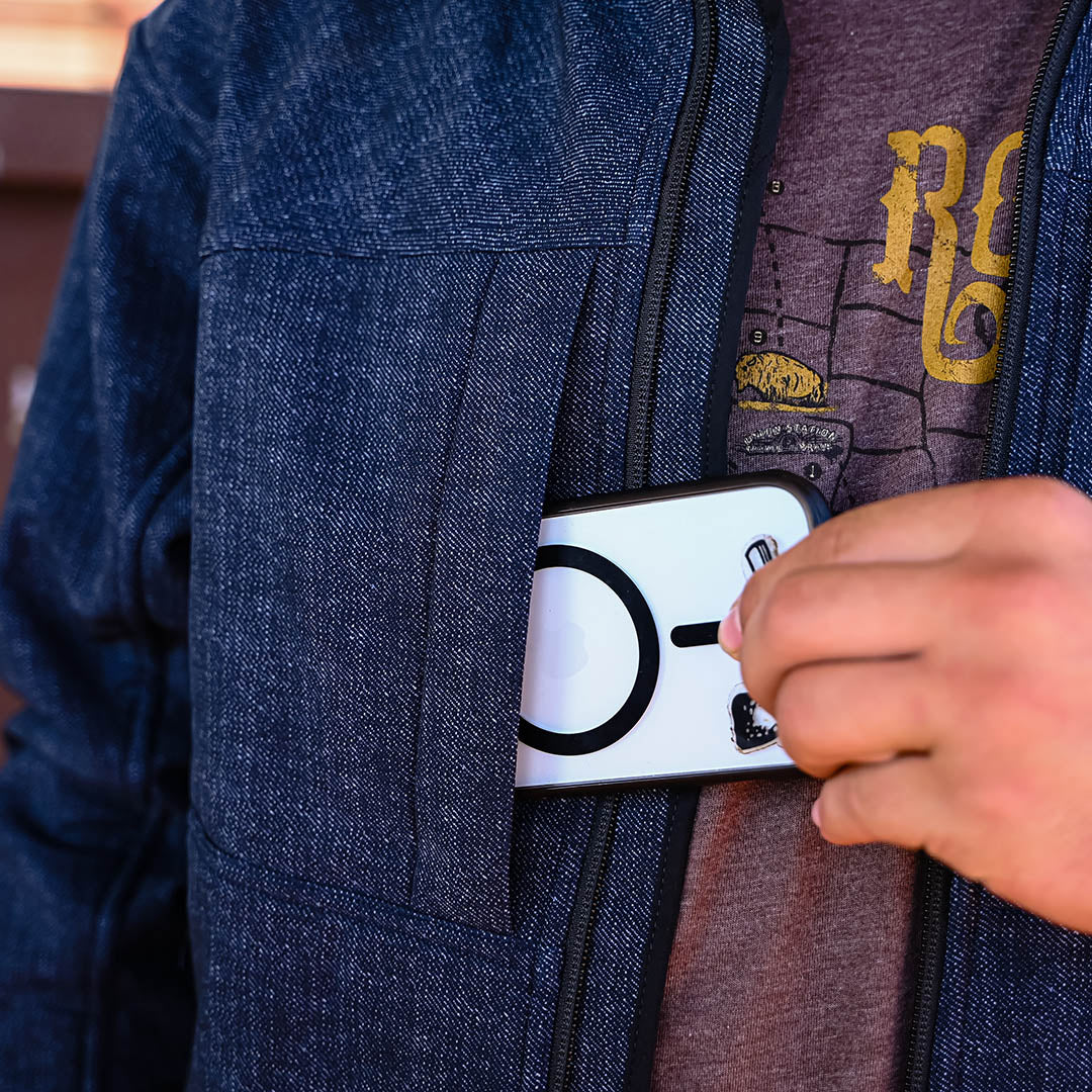 Person sliding a cell phone into a chest pocket on a navy softshell jacket.