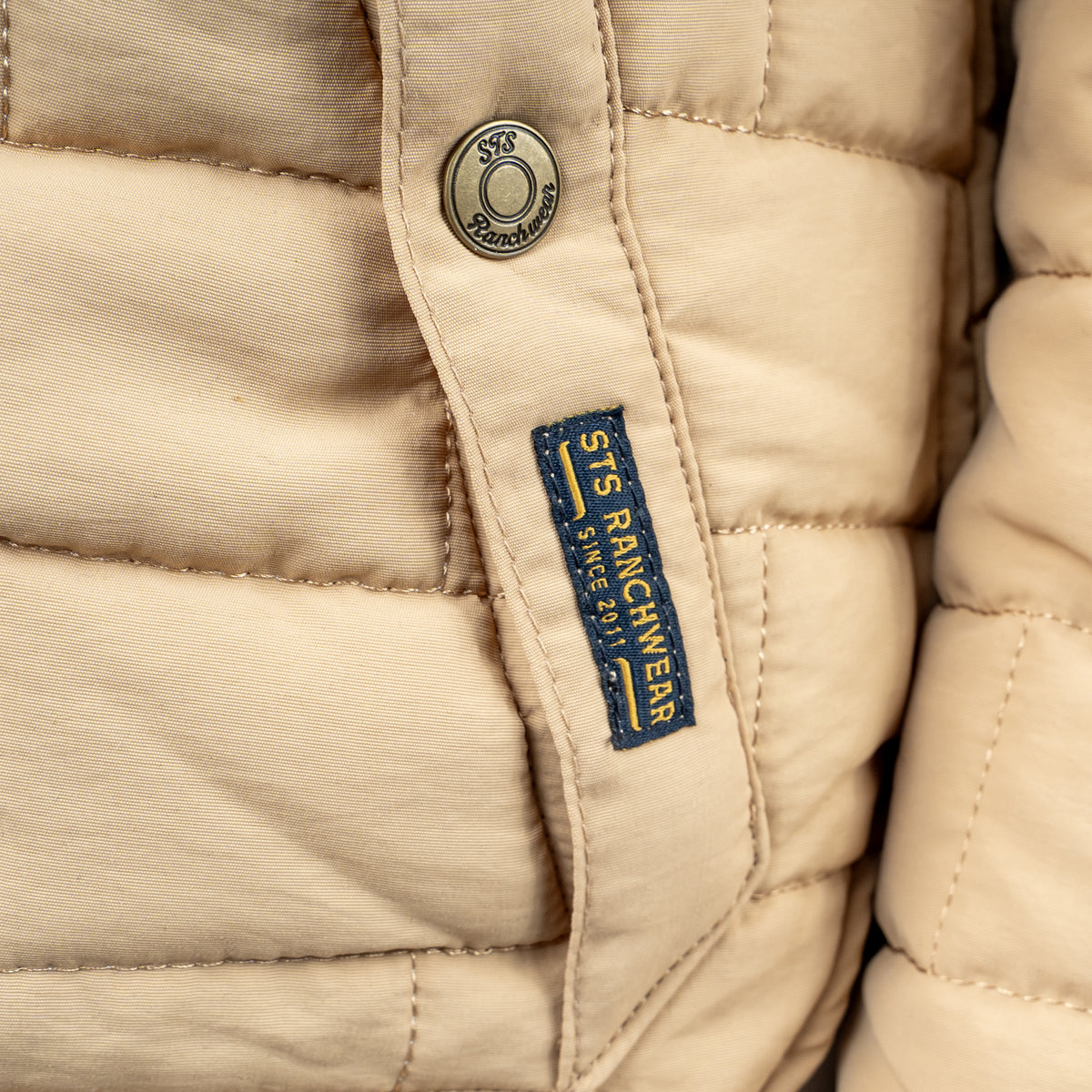 Closeup of the snap closure pocket on a quilted beige jacket.