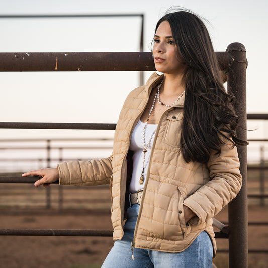Soni Vest wearing our quilted beige jacket with zip closure leaning against a metal fence.