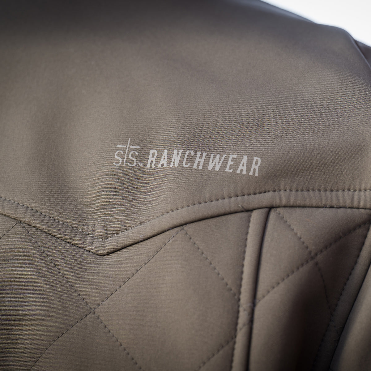 Closeup of the sts branding on the back shoulder of our olive green jacket.