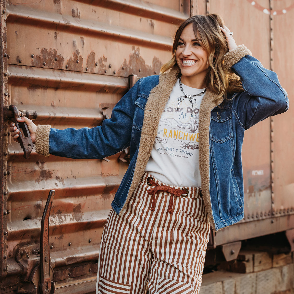Chenae Vest wearing a light wash denim jacket lined with sherpa, two chest pockets and front button closure jacket outside of metal doors.