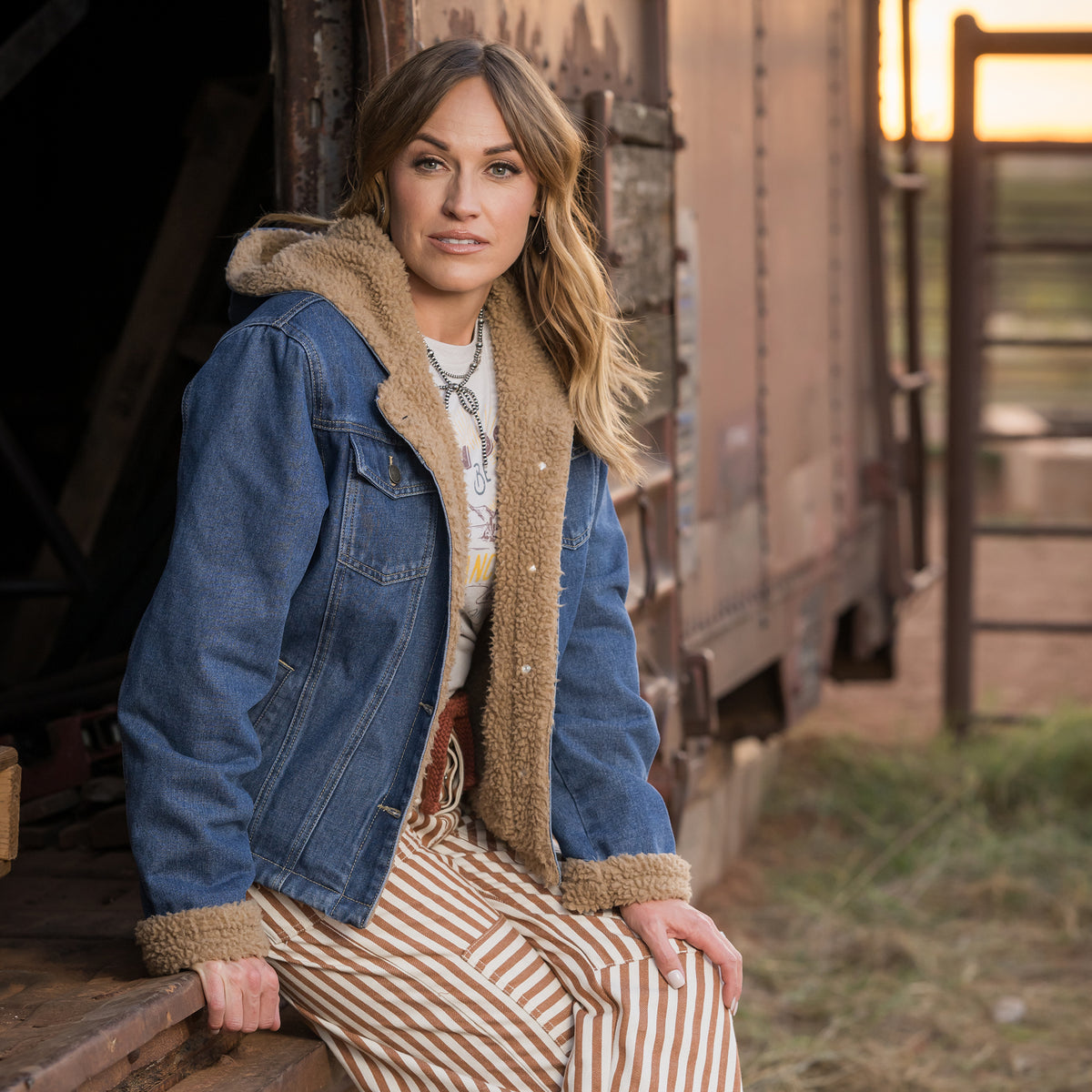 Chenae Vest wearing our light wash denim lined with sherpa, two chest pockets and front button closure jacket outside of metal doors