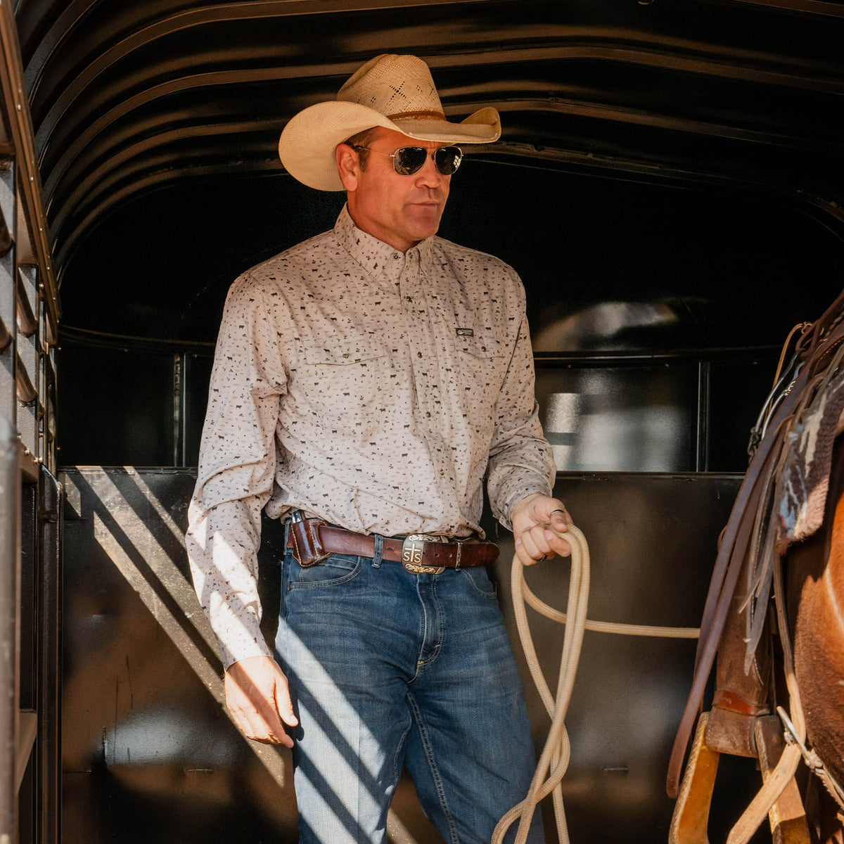 Stran T Smith standing in a horse trailer wearing a tan cowboy hat, jeans, sunglasses and a khaki pearl snap long sleeve shirt.
