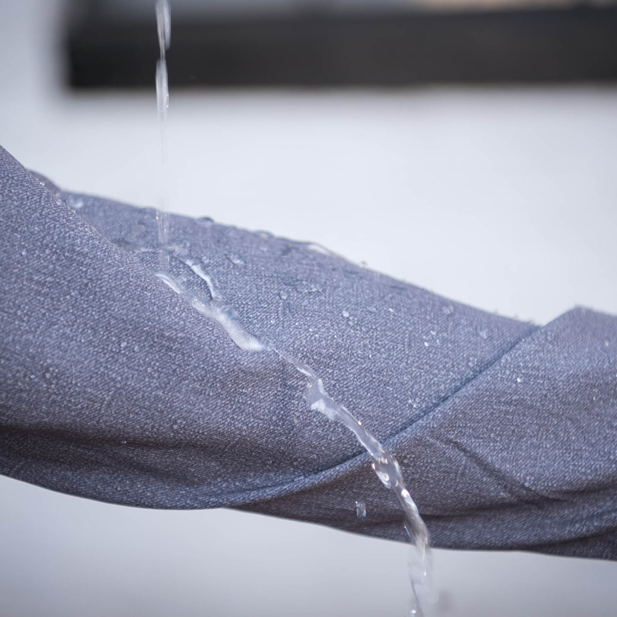 Detail of water dripping off sleeve of a heather gray men's rain jacket.