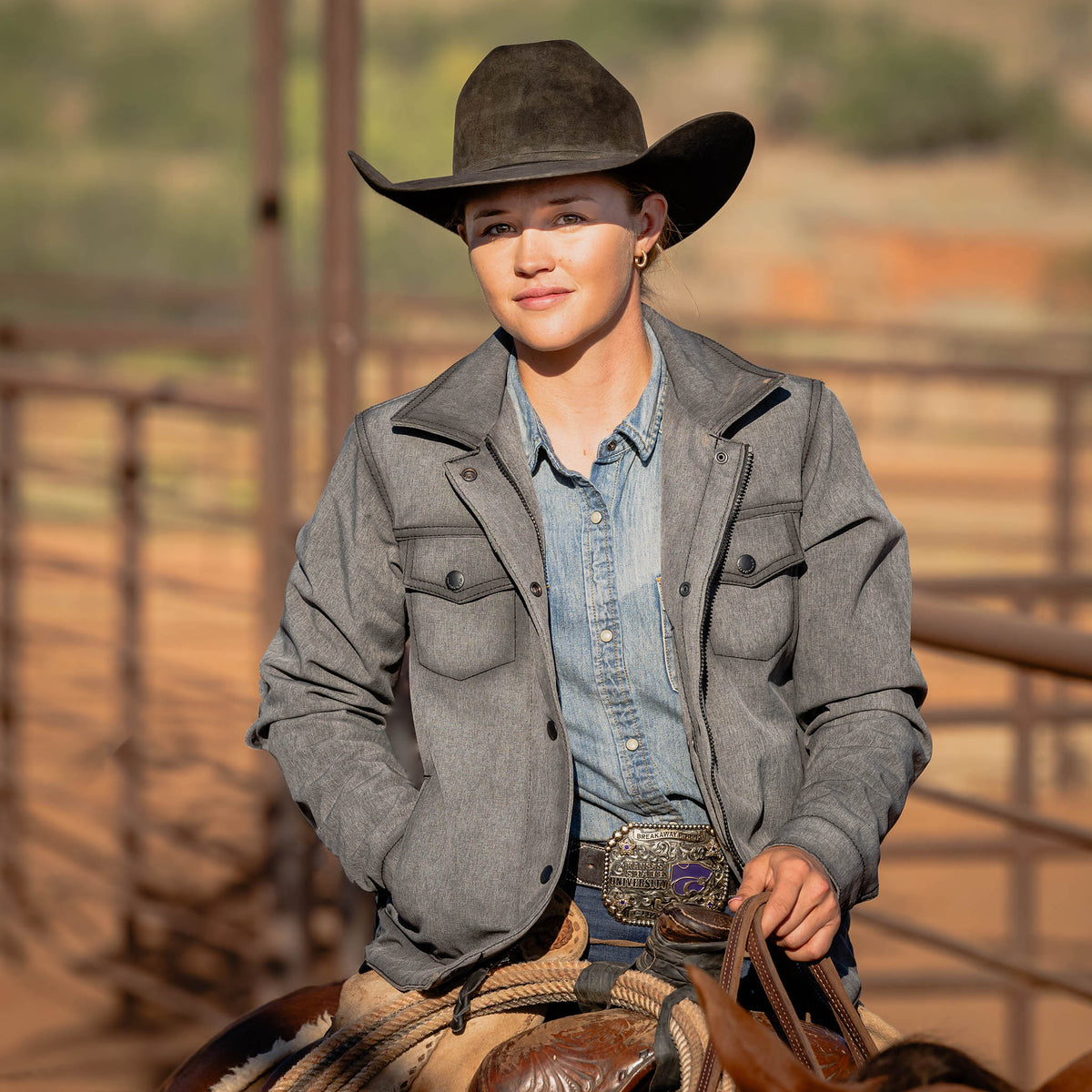 Woman sitting on a horse wearing a black cowboy hat, denim shirt and gray softshell jacket.
