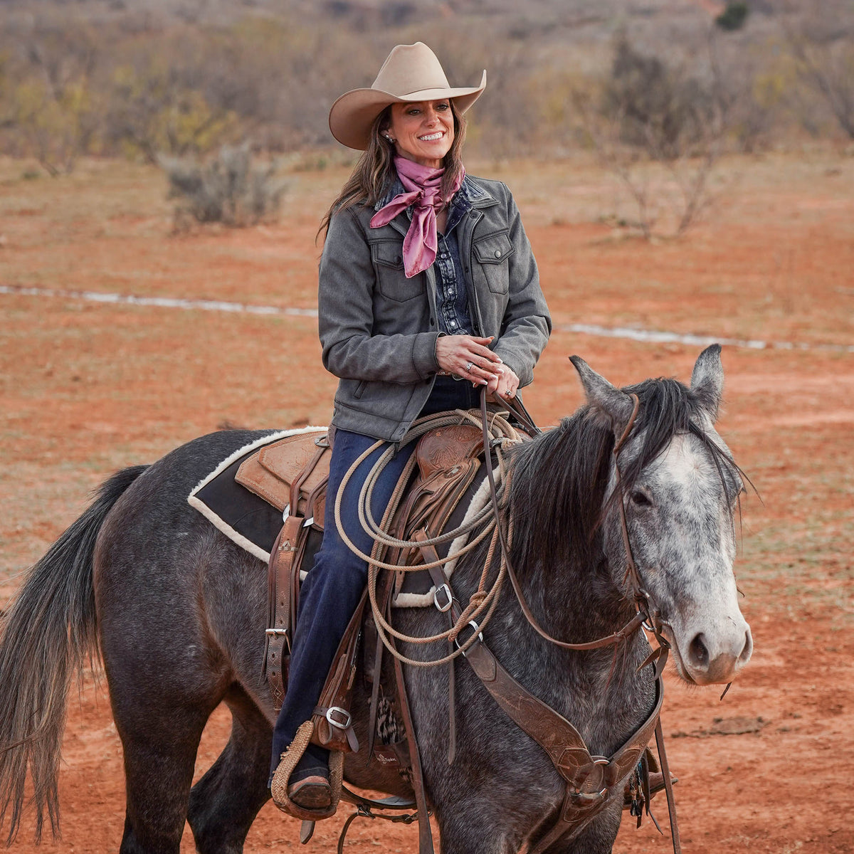 Jen Smith sitting on a horse wearing a tan cowboy hat, jeans, pink scarf and gray softshell jacket.