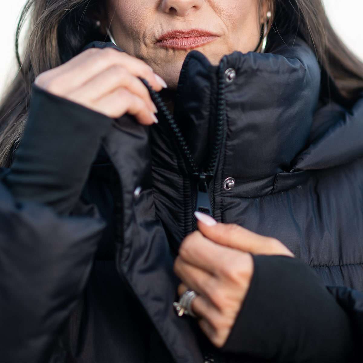 Close up of a woman zipping a black puffer parka coat closed.