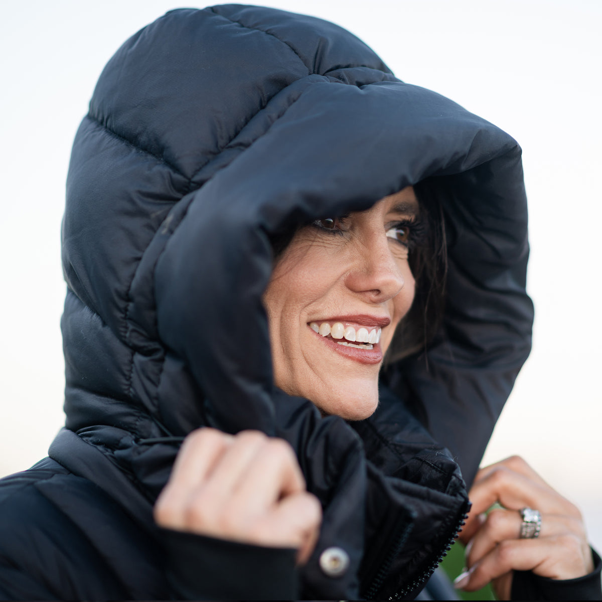 Woman with the hood of a black puffer parka coat over her head.