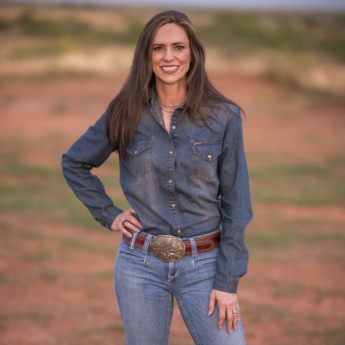 Jen Smith standing in a field wearing blue jeans and a denim pearl snap long sleeve shirt.