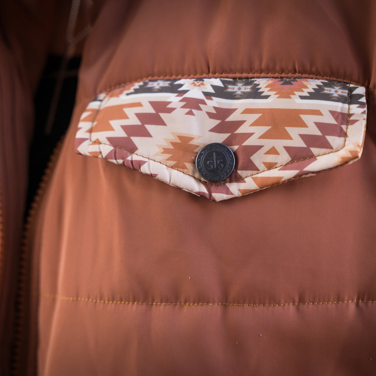 Closeup of the front pocket of our rust collared puffer jacket with aztec detailing and snap closure.