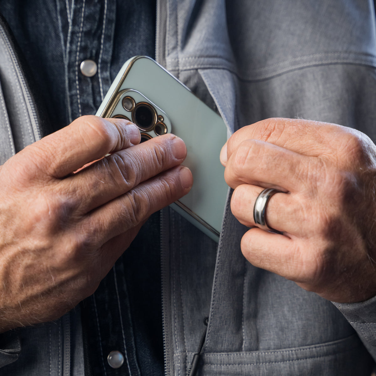 closeup of a phone being put into the inside pocket of our gray jacket with zip closure, removable hood and hand warming pockets