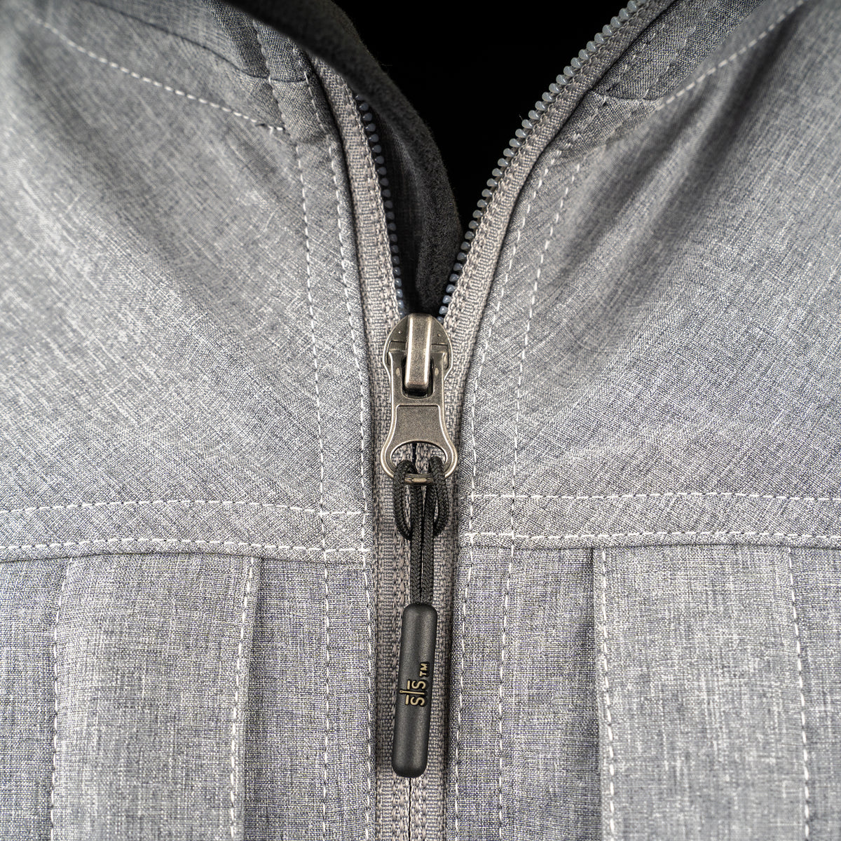 closeup of the front zipper on our gray jacket with zip closure, removable hood and hand warming pockets on white background