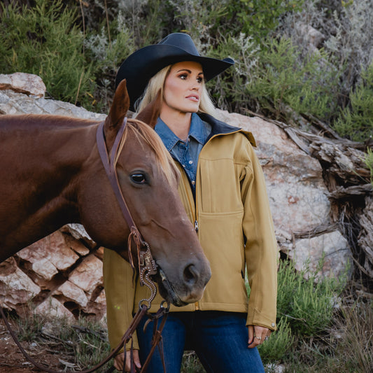 Terryn Cooper wearing our curry yellow jacket with zip closure, removable hood and hand warming pockets next to a brown horse outside