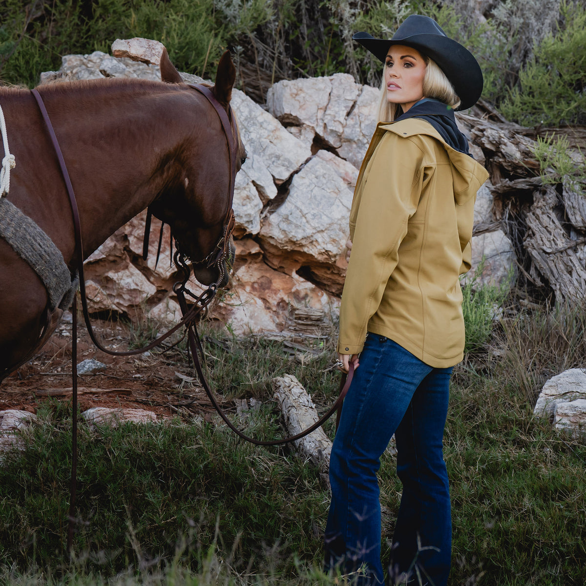 Terryn Vest next to a brown horse wearing our curry yellow jacket with zip closure, removable hood and hand warming pockets
