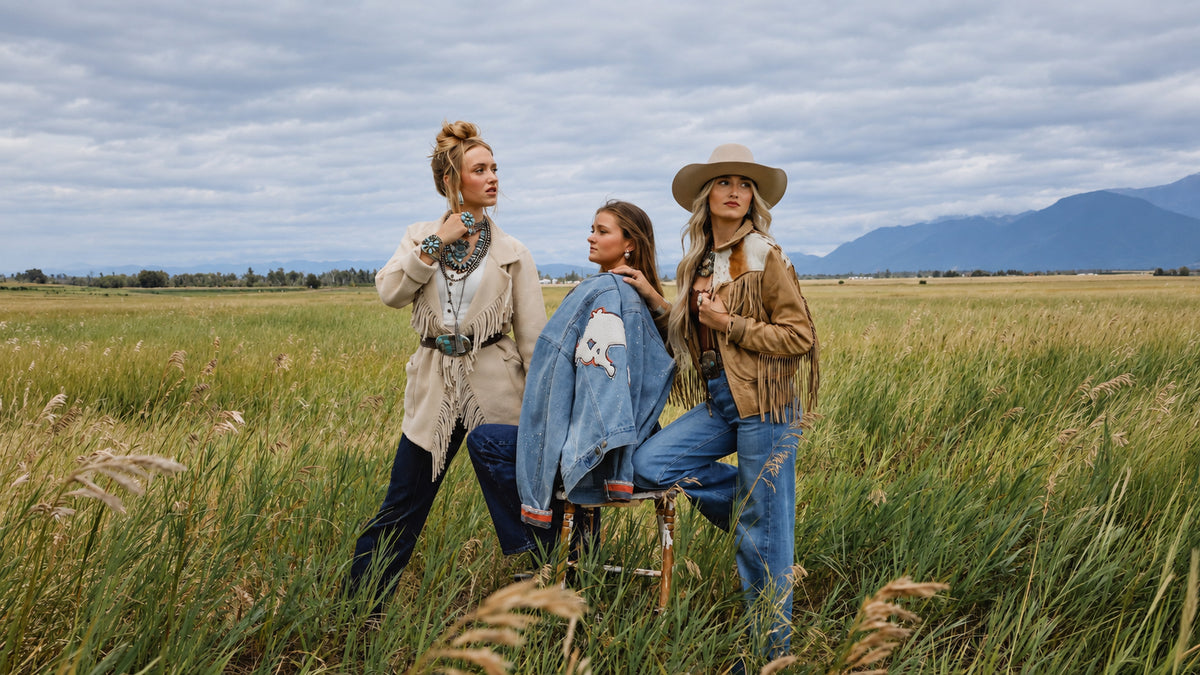 Three women standing in a field with mountains behind them.