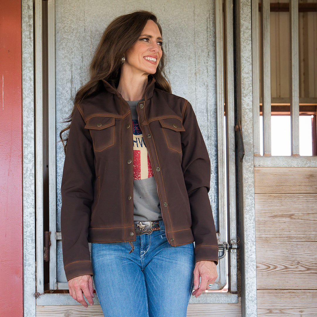 Jen Smith wearing a brown softshell jacket and blue jeans standing in a barn.