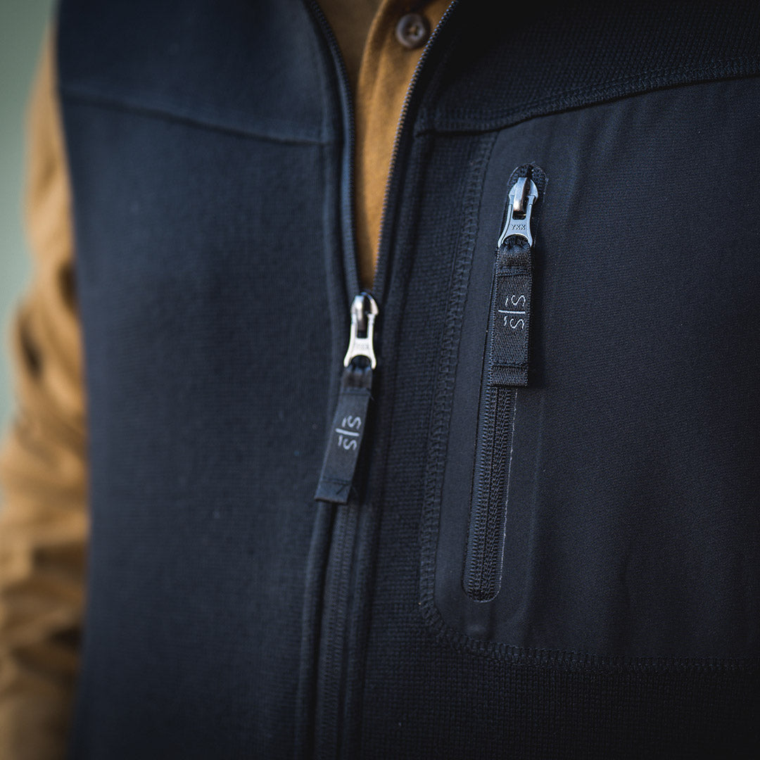 Two zippers with STS zipper pulls on the front of a black softshell vest.