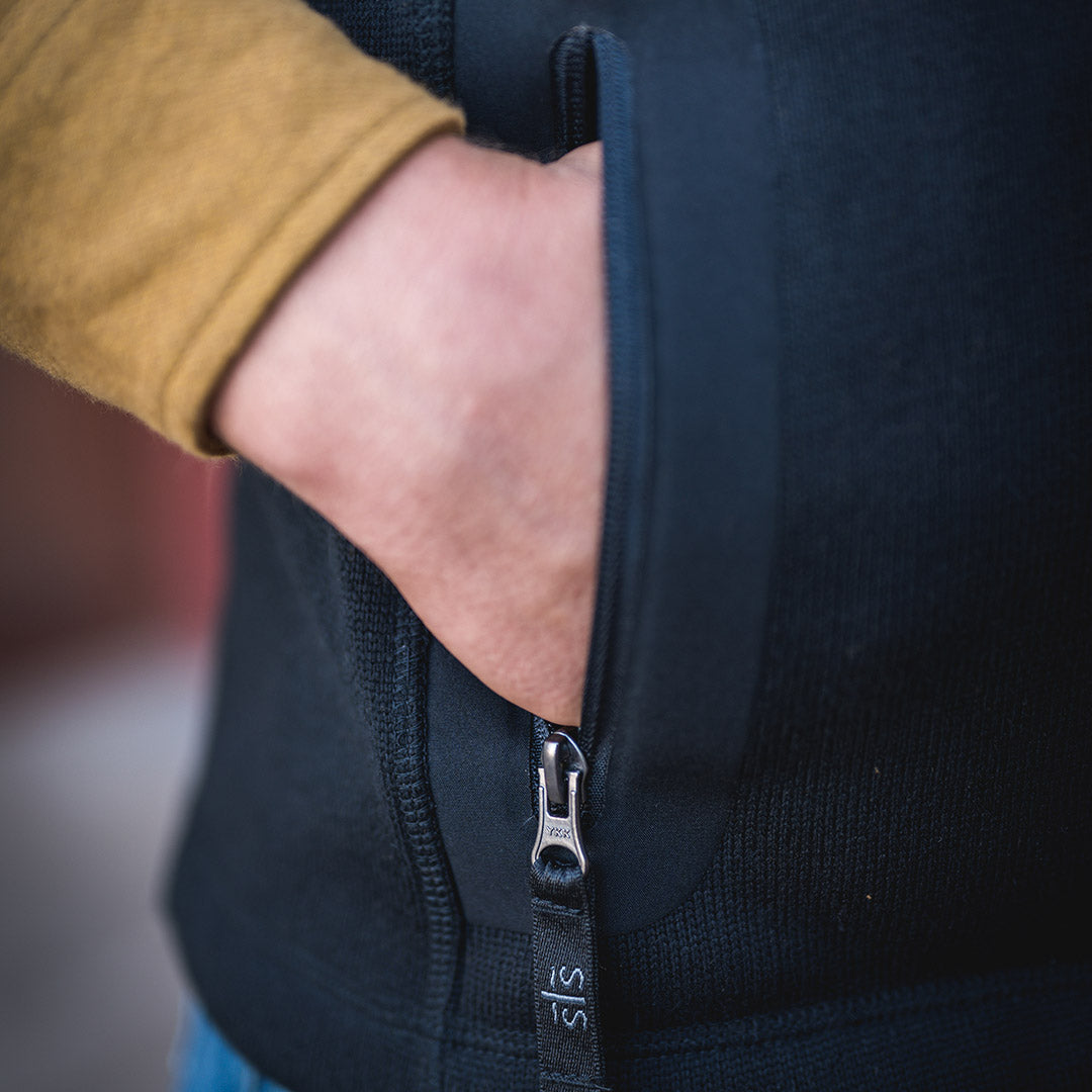 Person with their hand in the zip closure pocket on a black softshell vest.