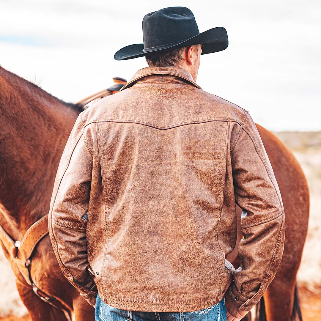 Man facing away standing in front of a horse wearing a black cowboy hat and brown genuine leather jacket with a western yoke.