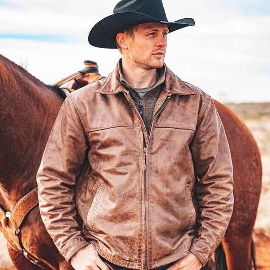 Man standing in front of a horse wearing a black cowboy hat and brown genuine leather zip closure jacket.