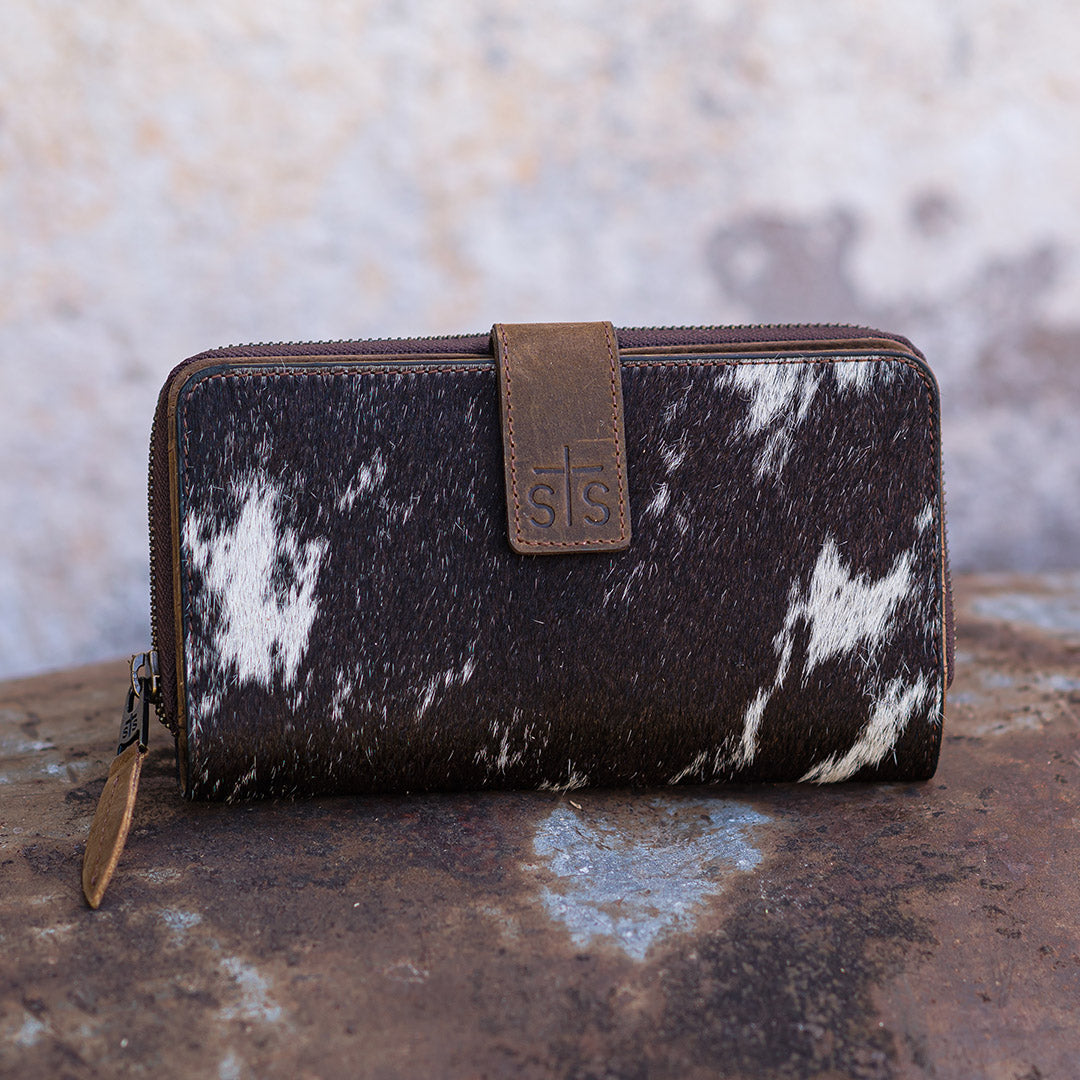 Brown and white cowhide wallet with leather tab with STS logo and zip around closure on a white background.