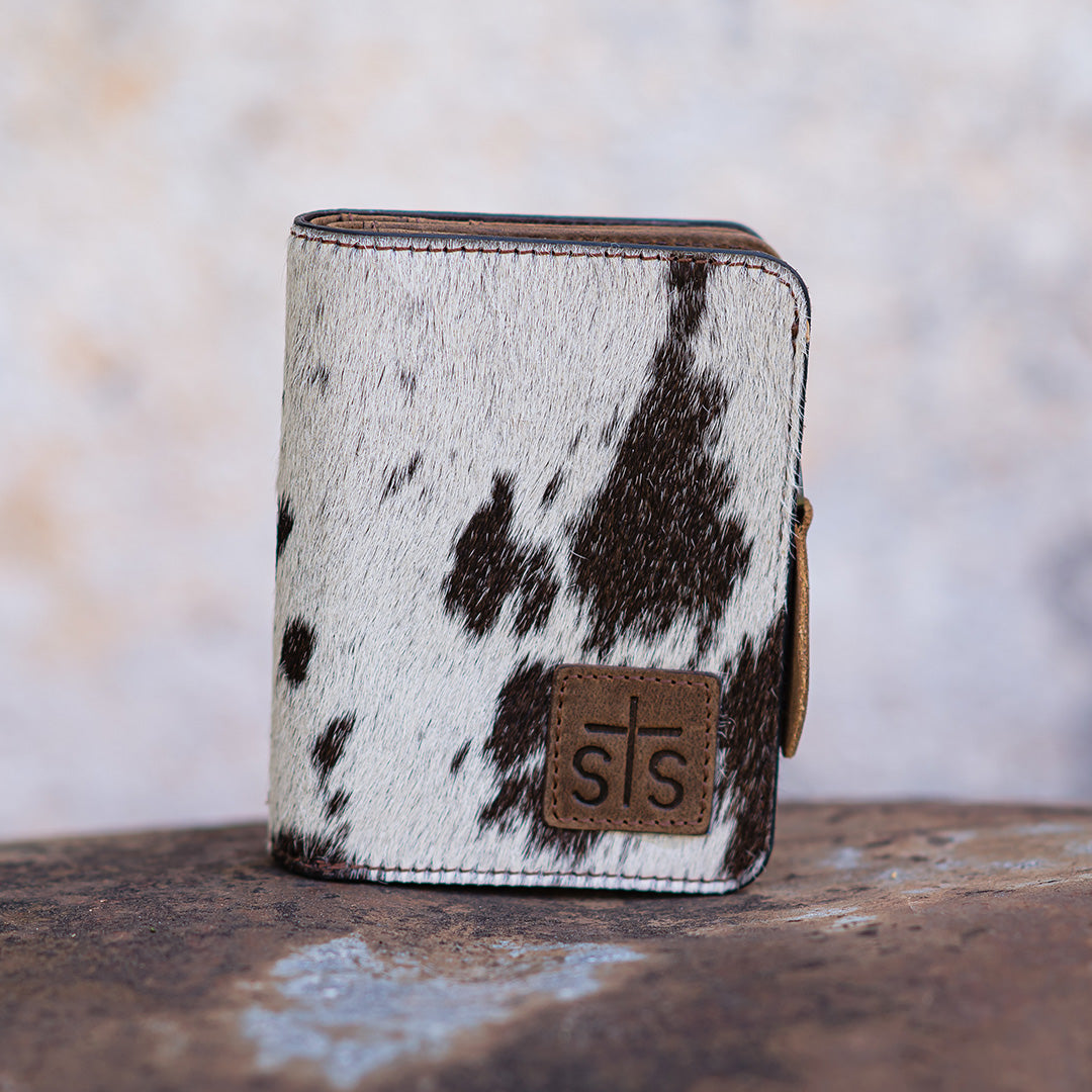 A wallet with brown and white hair on hide cowhide, zip around closure and brown leather patch with STS logo embossed.