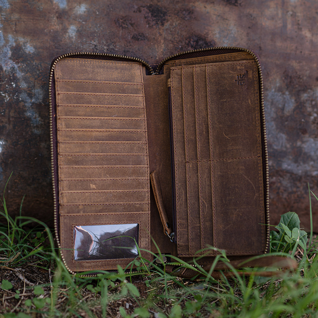 Inside of cowhide Bentley wallet with zip around closure, 1 ID slot and card slots leaning against a building in the grass.
