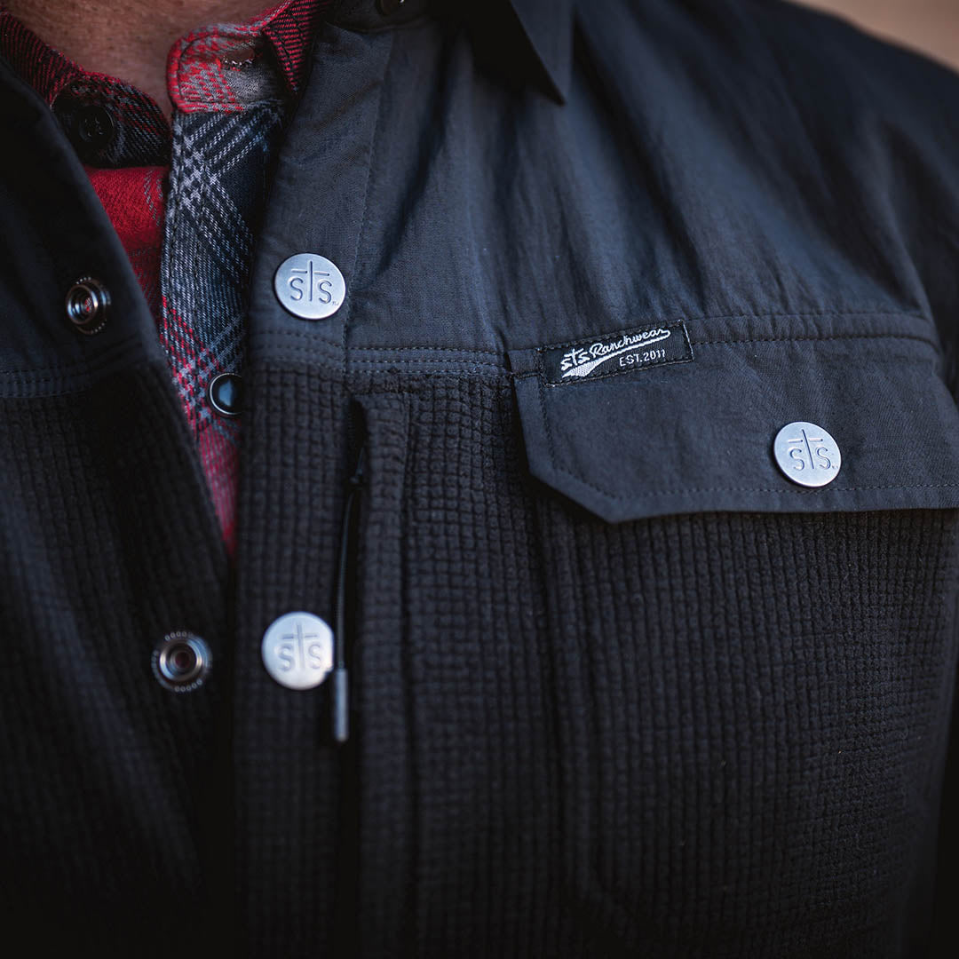 Front closure buttons with STS stamped on them on the front of a black button up shirt.