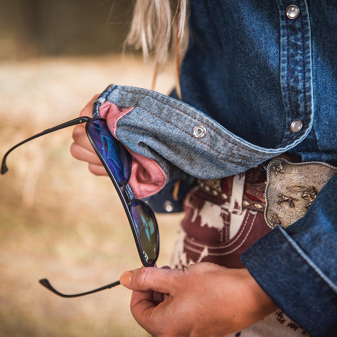 Person cleaning their sunglasses using the Women's Rod denim shirt cloth cleaner.