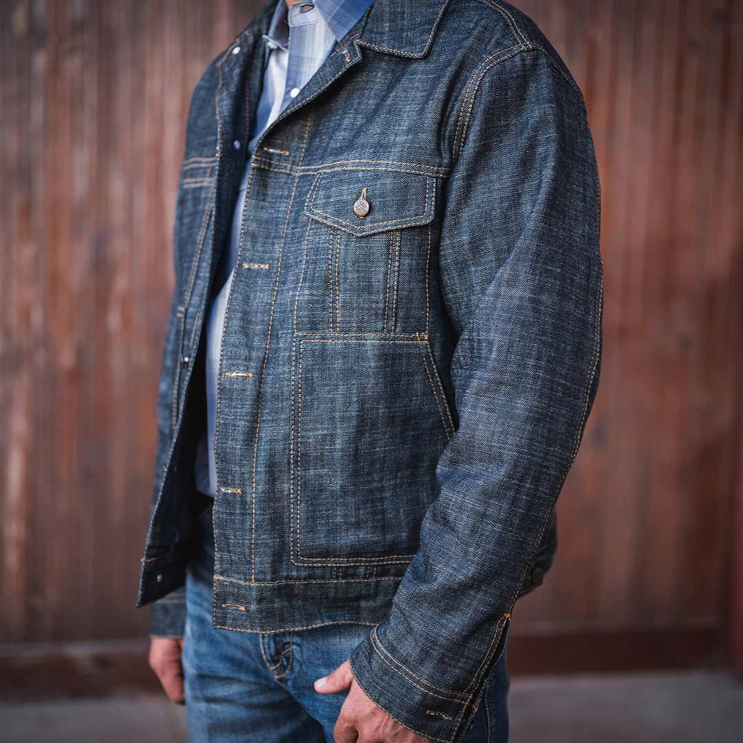Person wearing a denim jacket standing in front of a wooden wall.